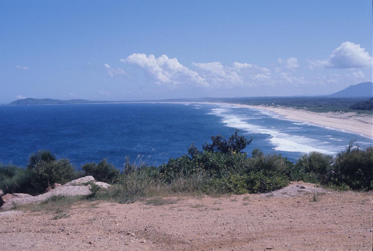 From headland, looking over sandy beach with breaking waves, to distant headland