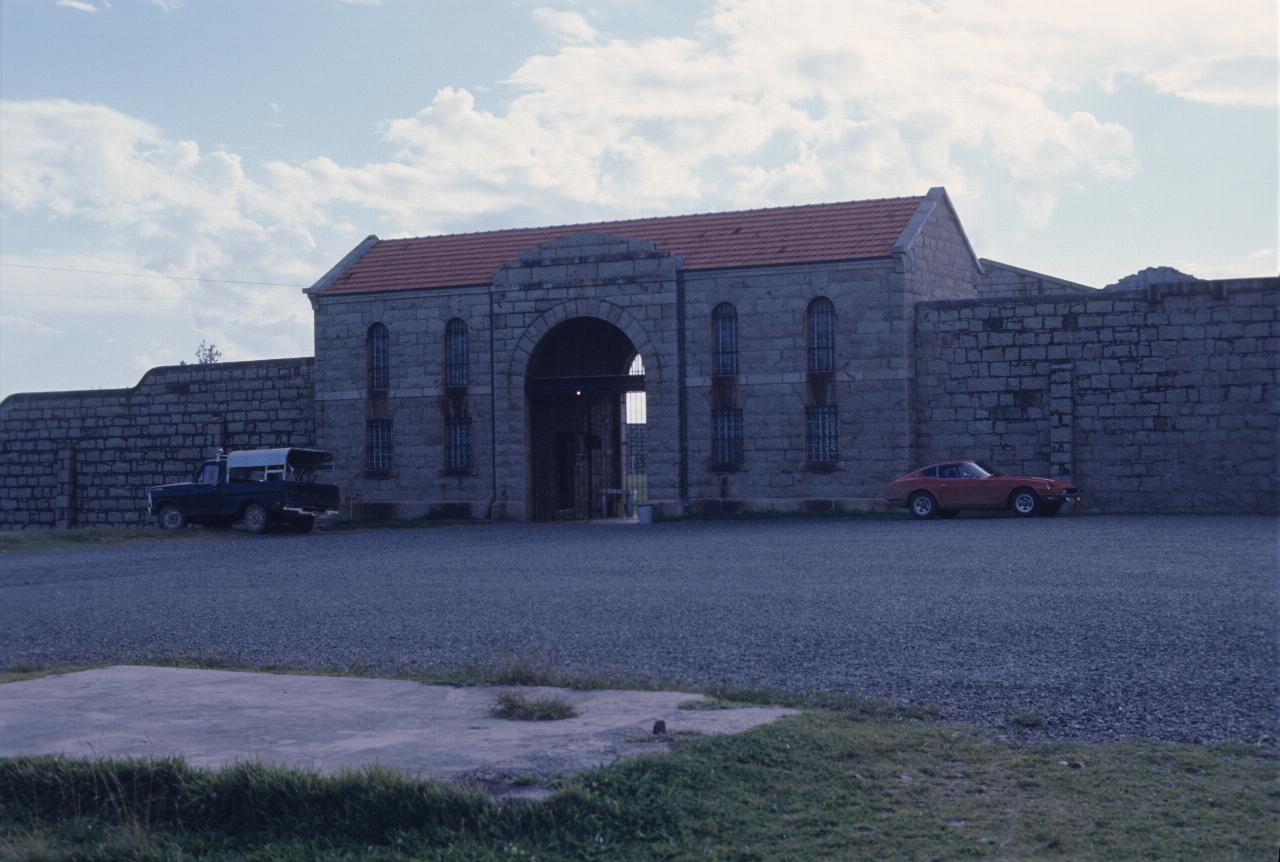 Stone building with barred windows, arched entryway, stone walls on both sides