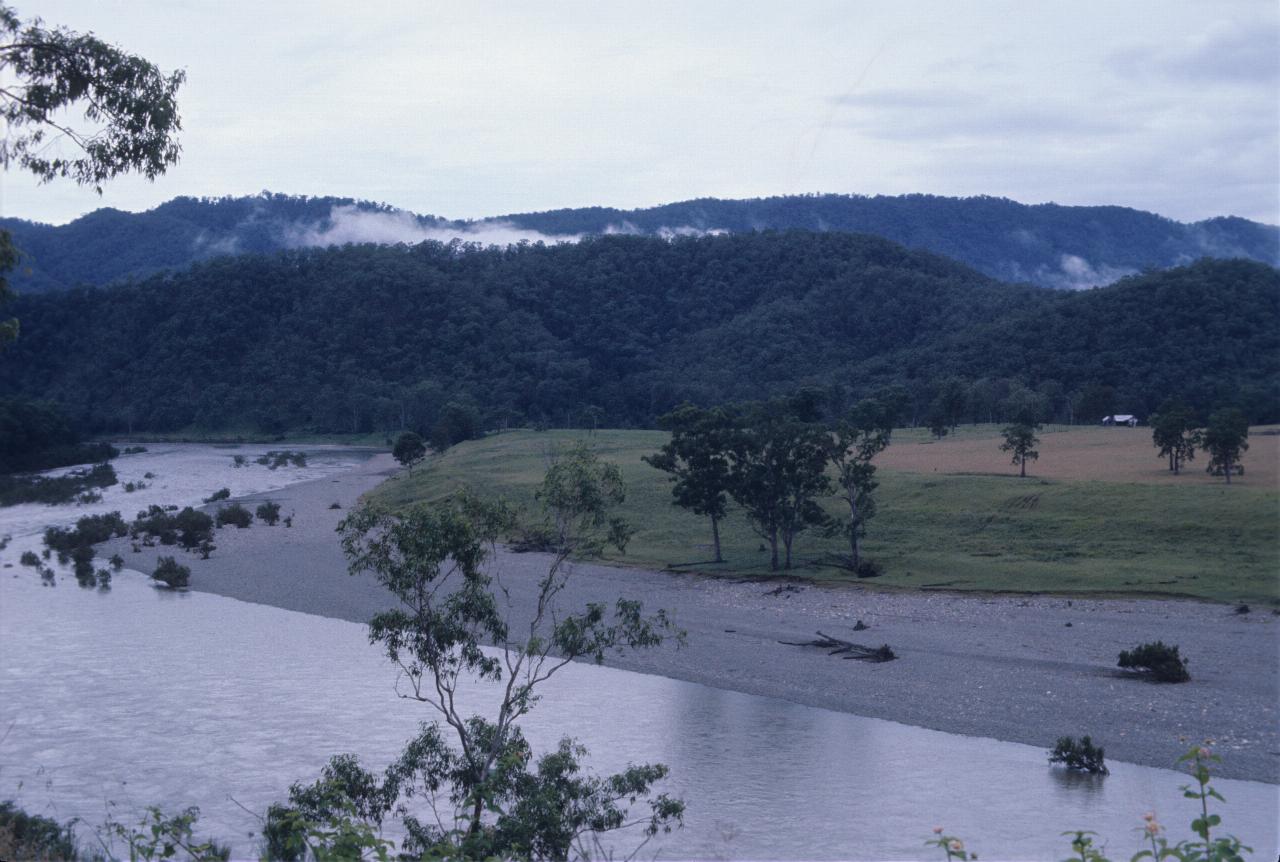 Broad, shallow river with farmland then hills with low clouds behind