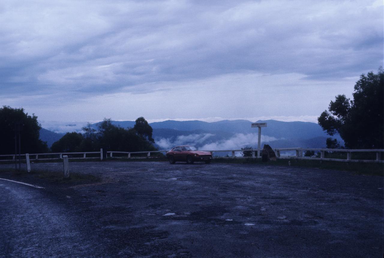 Car sitting in parking area, mountains and low cloud behind