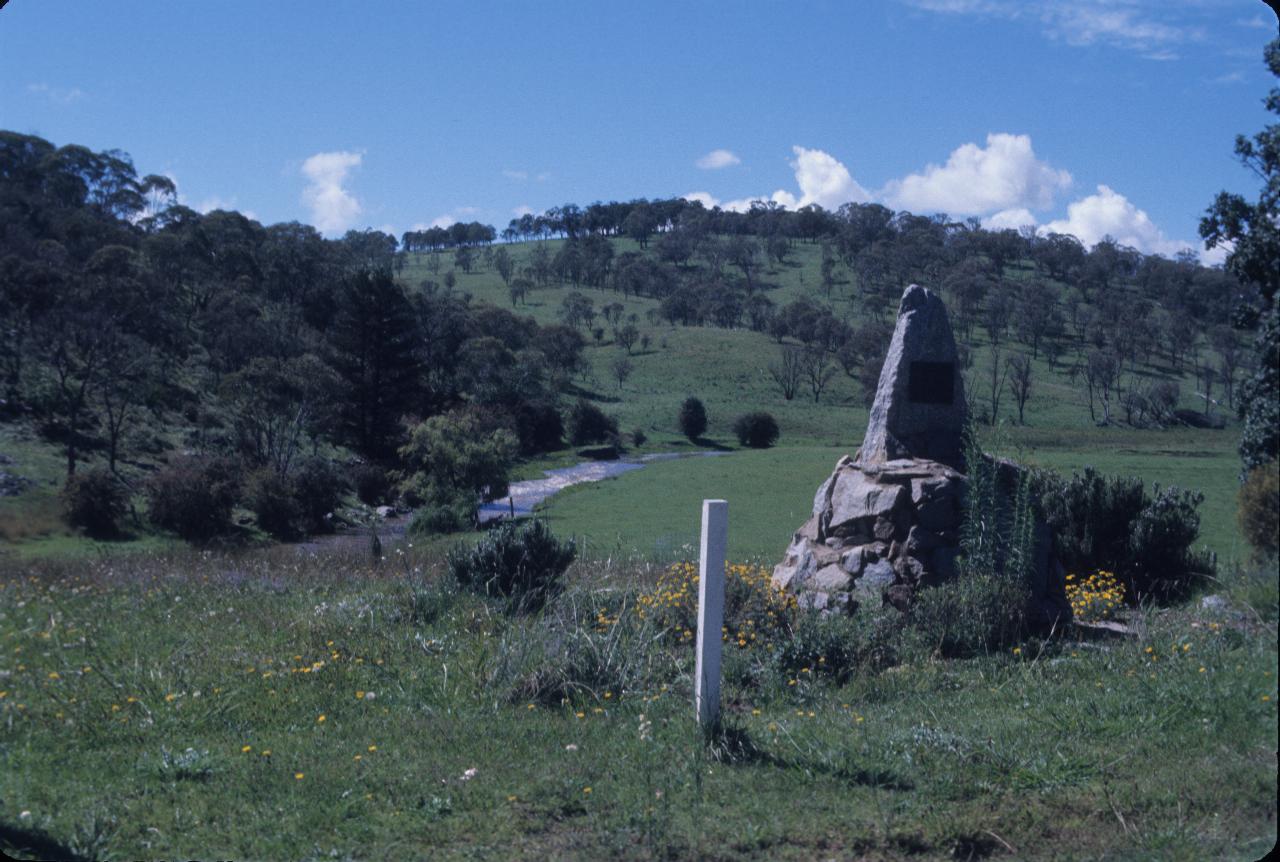 Stone cairn on side of road, overlooking small stream and grassland