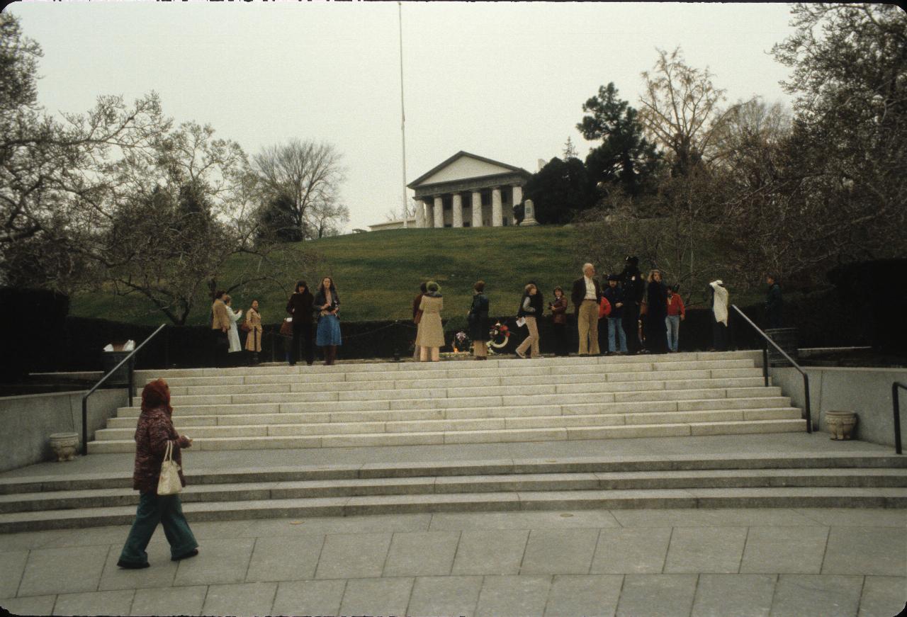 White steps leading to area with people, thence grassy hill to imposing mansion with marble pillars