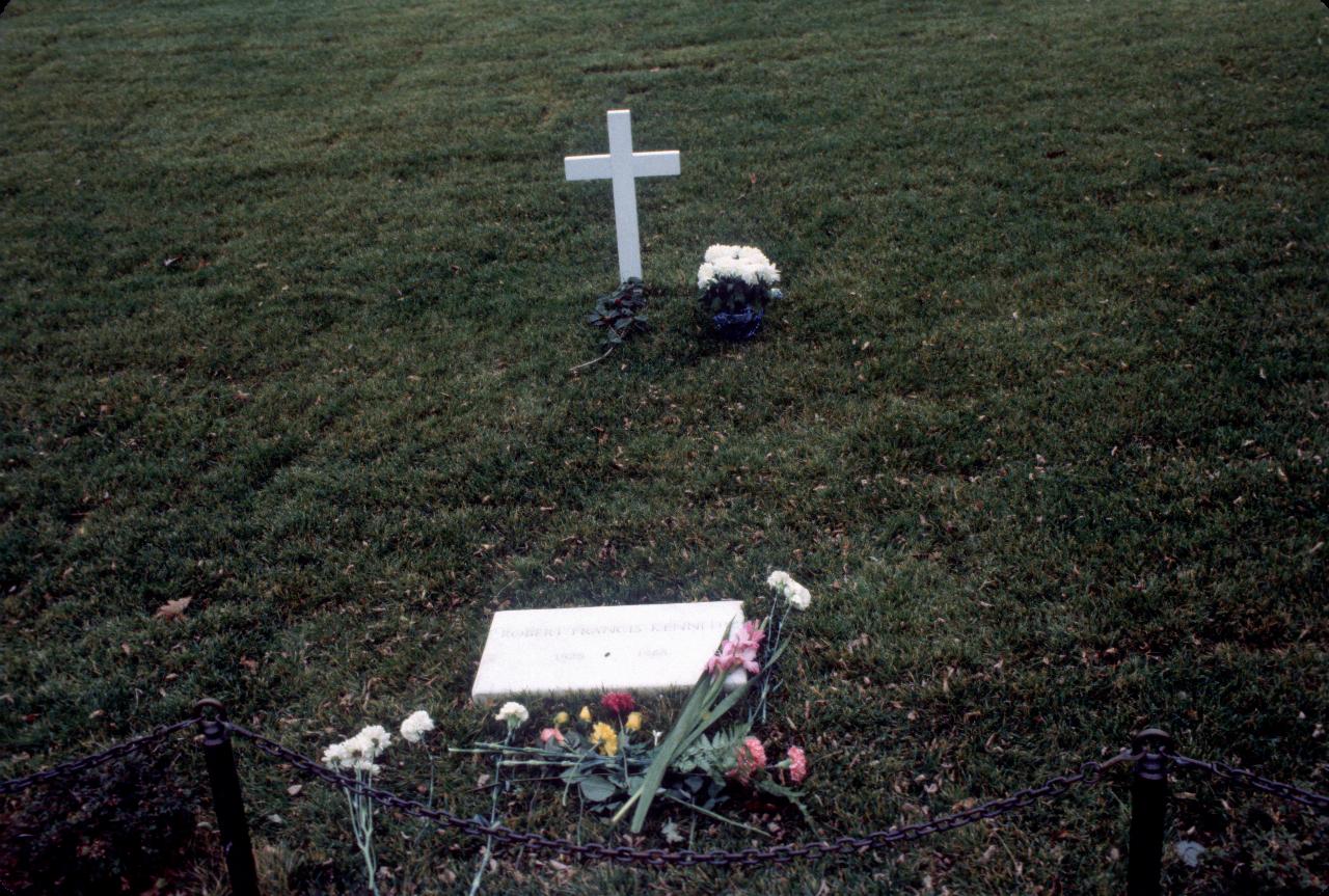 Small white cross, with a few flowers and white marble grave marker