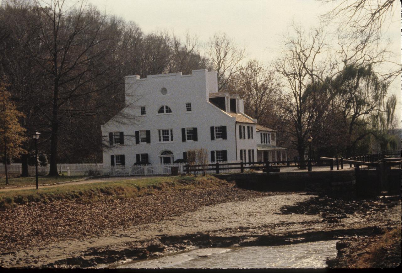 Large, three storey white building at a canal loch; trees behind, empty canal in front