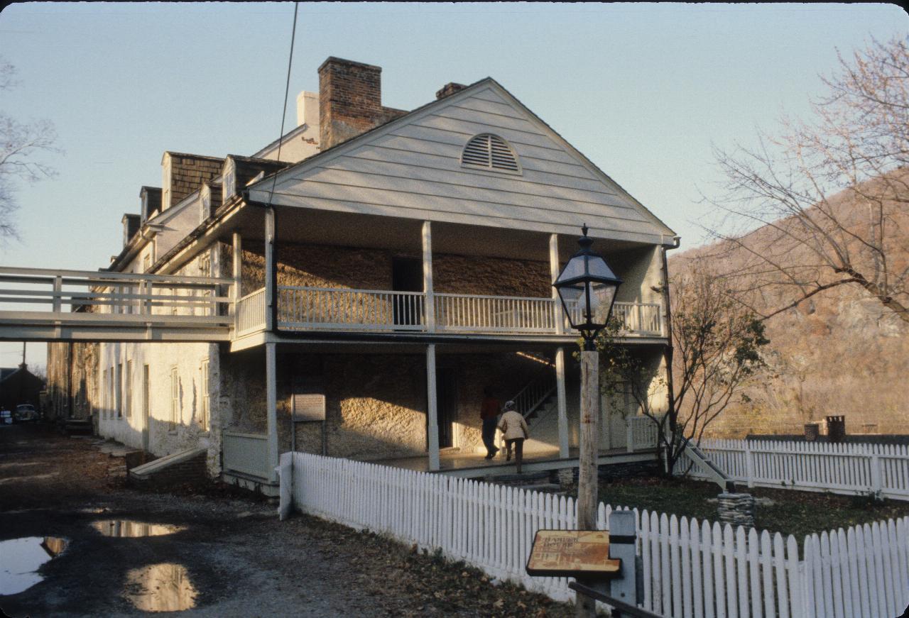 Stone and wood two storey house, with picket fence around a small yard