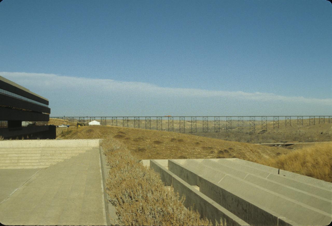 Cement structures in the foreground, looking along the coulee to a high railway trestle crossing it