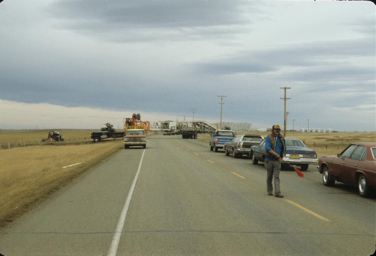 Cars lined up waiting for large truck to back into a field