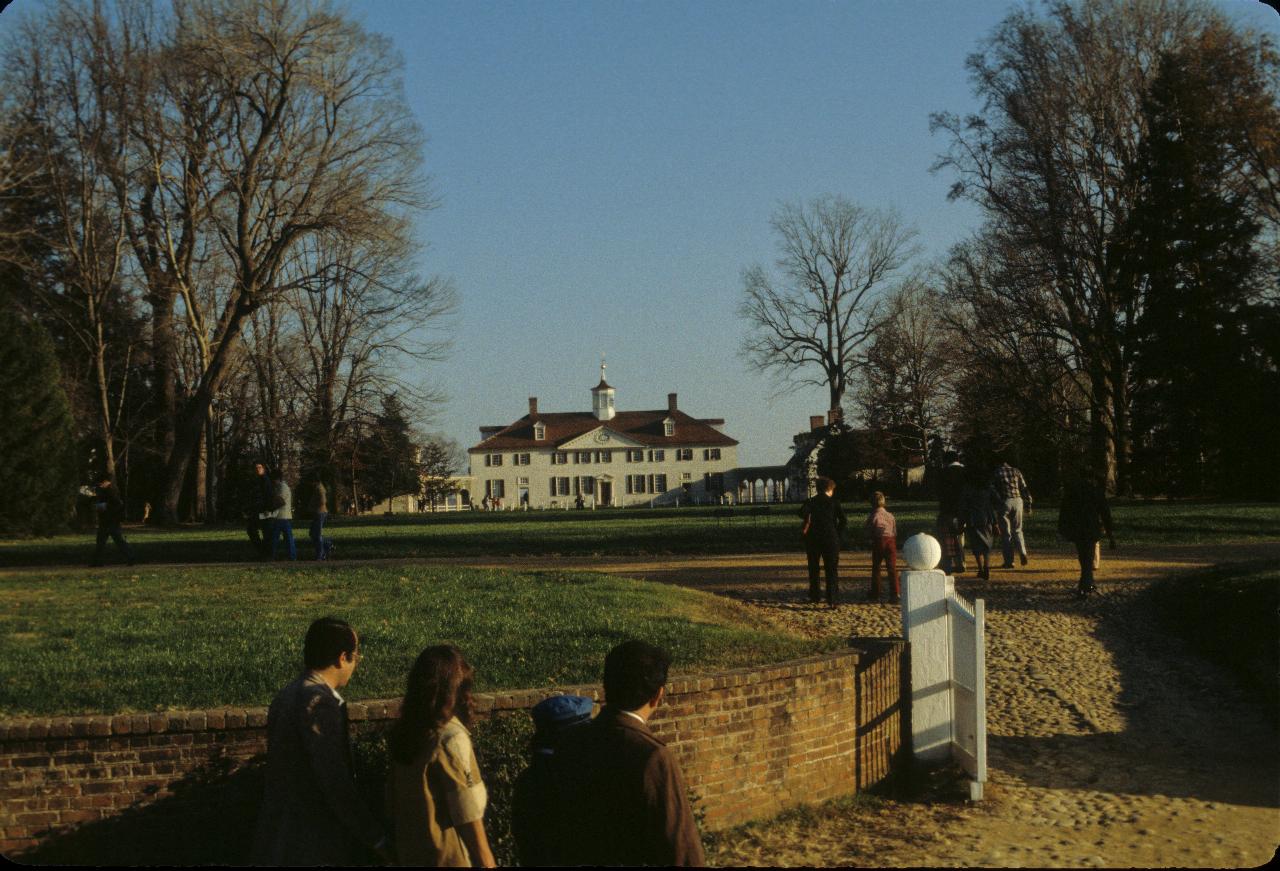 Gate and lawns leading to large white house with dark roof