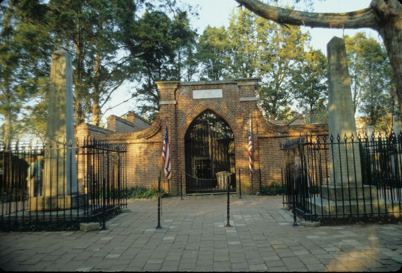 Two obelisks in front of brick wall with entrance into graves