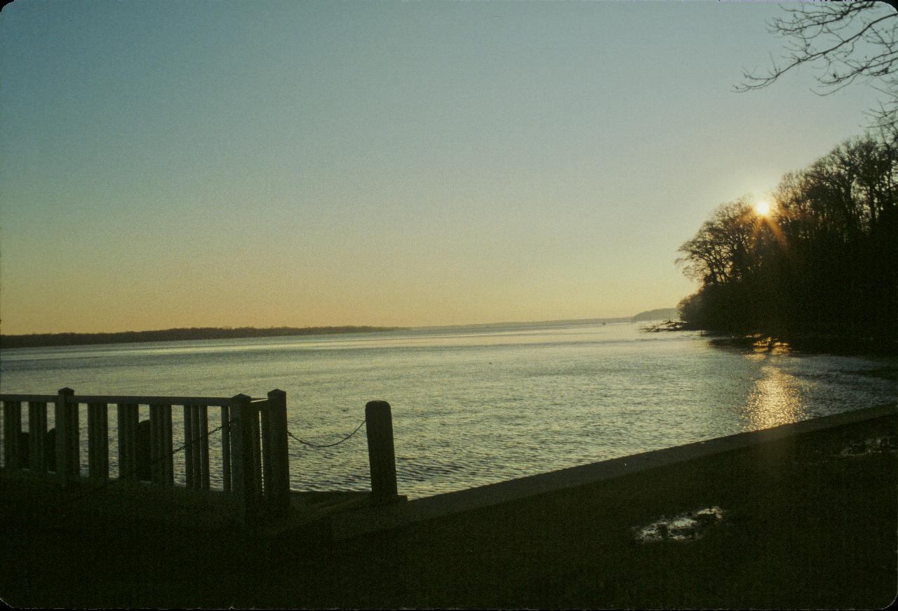 Large expanse of water, distant land and trees with sun setting behind