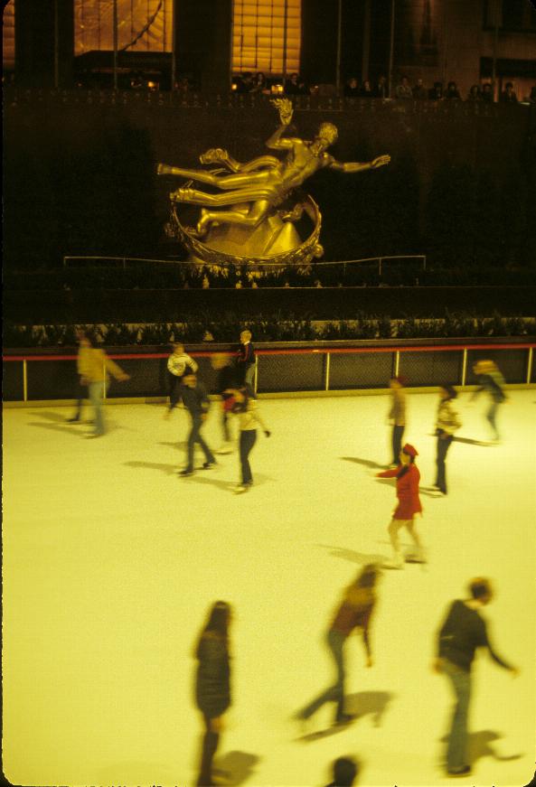 Ice skaters on a rink below a golden coloured statue