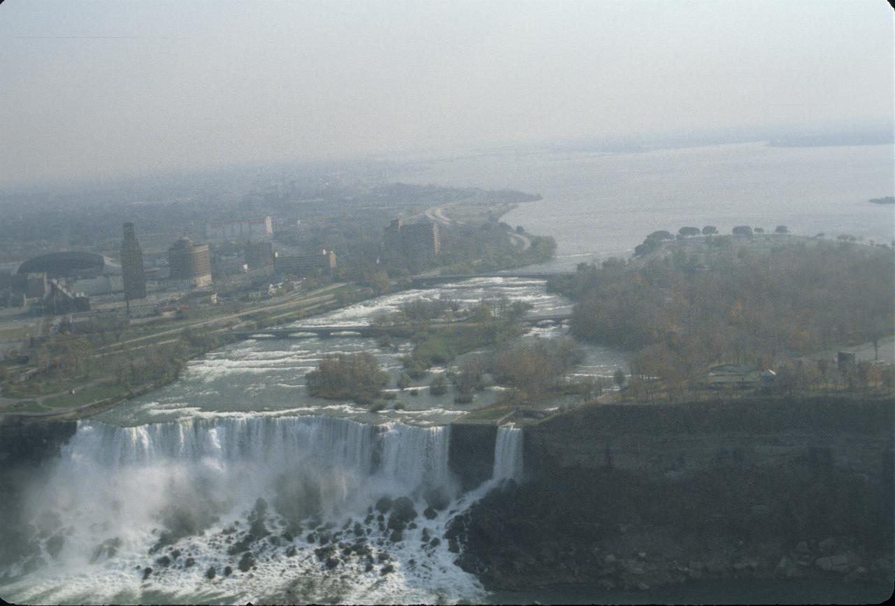 Waterfall from large lake into rocky area below, with city buildings to the left