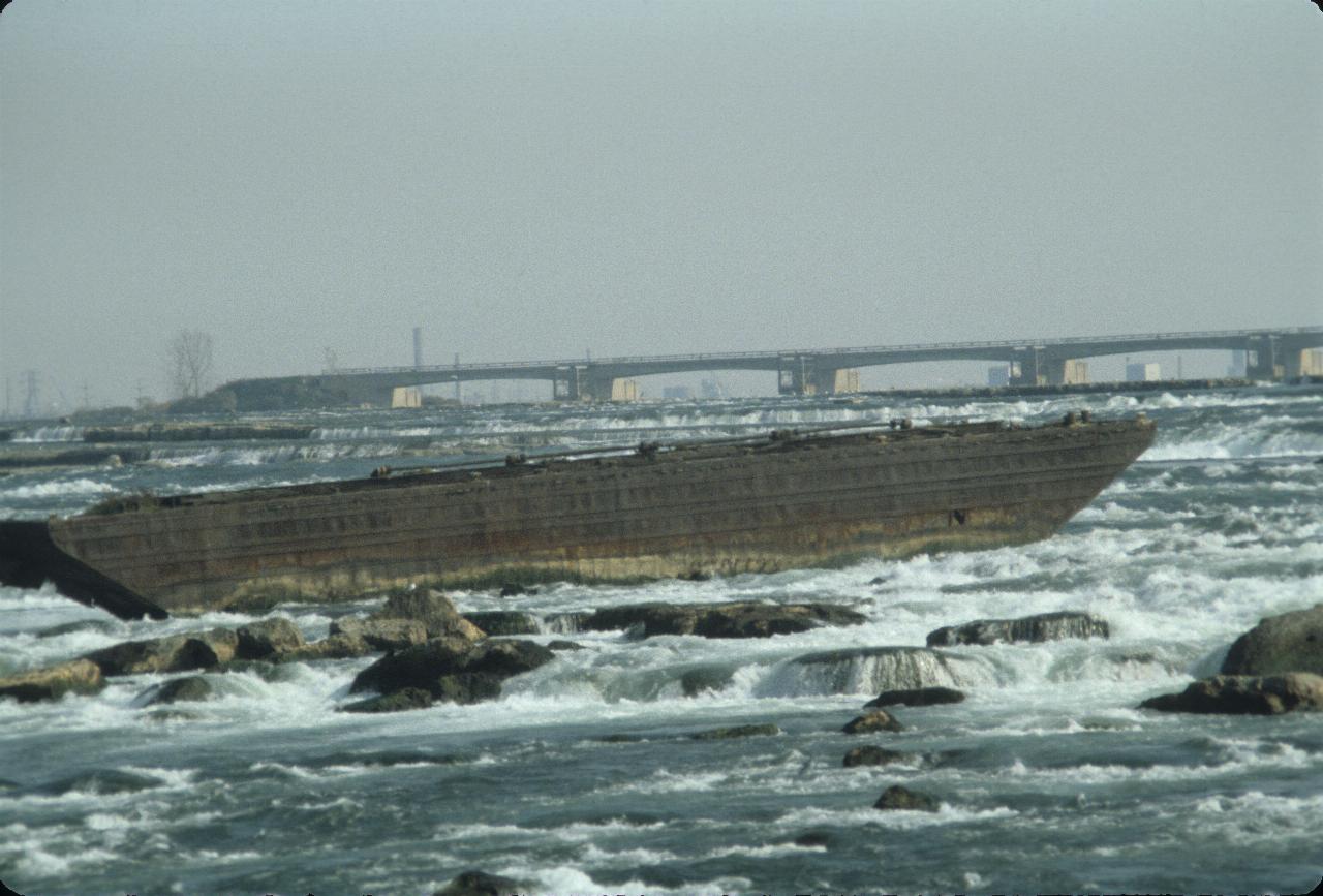 Rusting barge stuck on rocks in rapidly flowing river