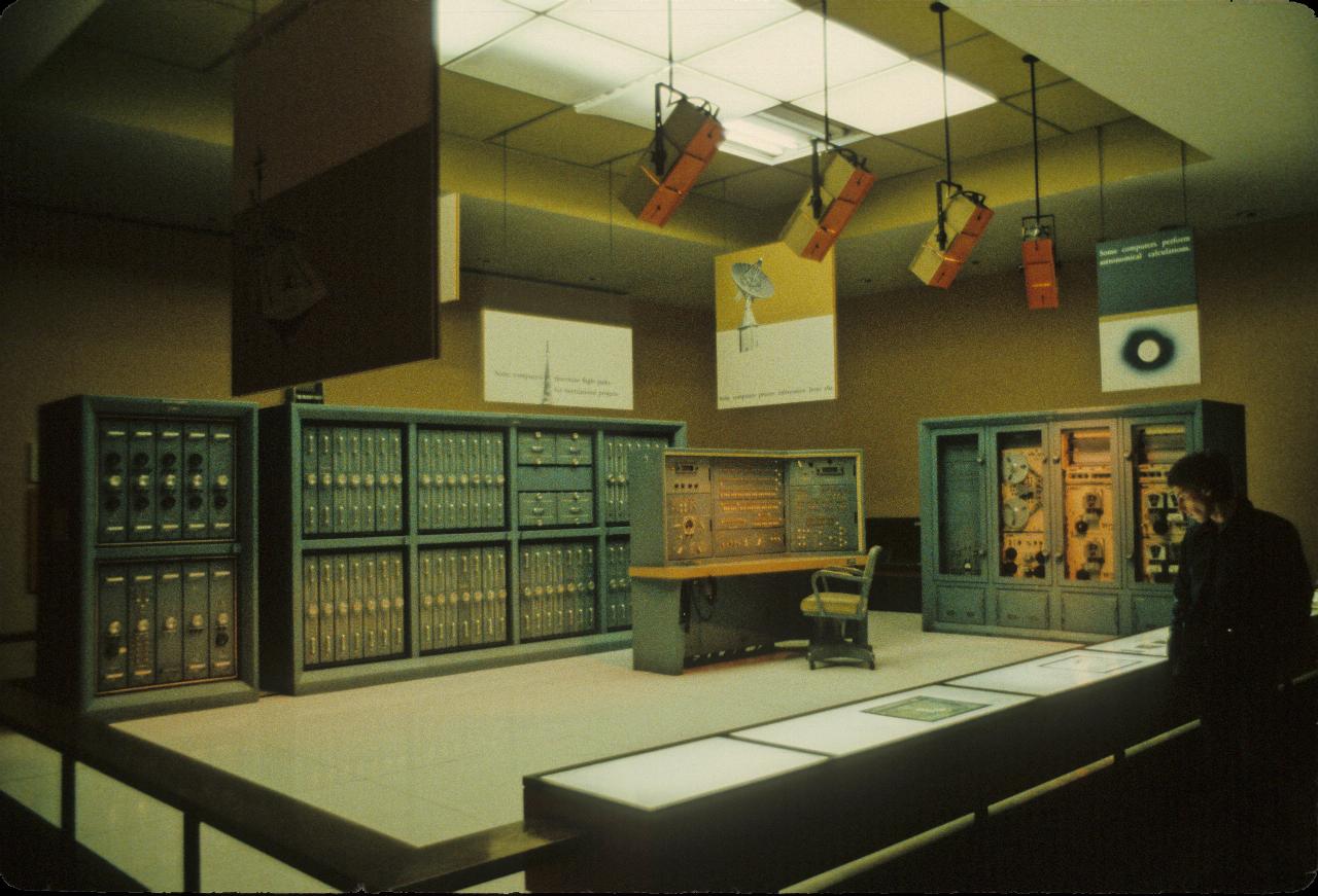 Squaer display area with racks of computer equipment around the two rear sides, and an operator's console in the middle