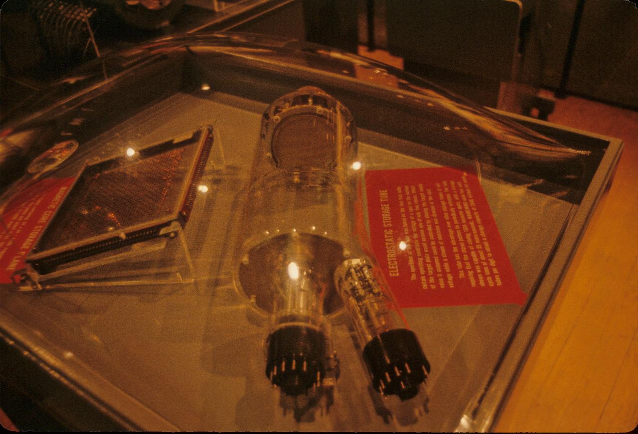 Display case with metal frame on left, and large glass tube in the middle