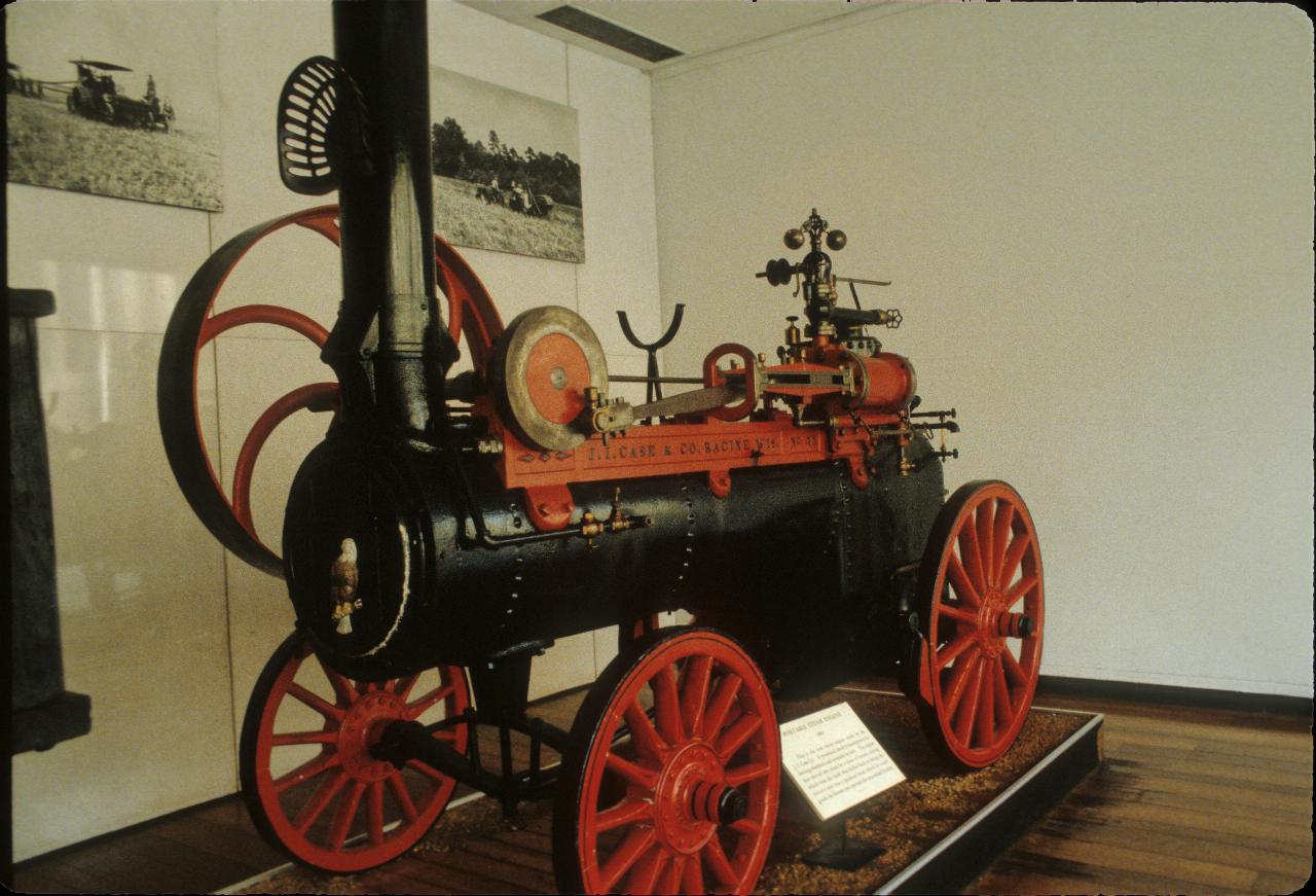 Black cylindrical boiler on red wheeled carriage with large diameter power take-off wheel and tall chimney