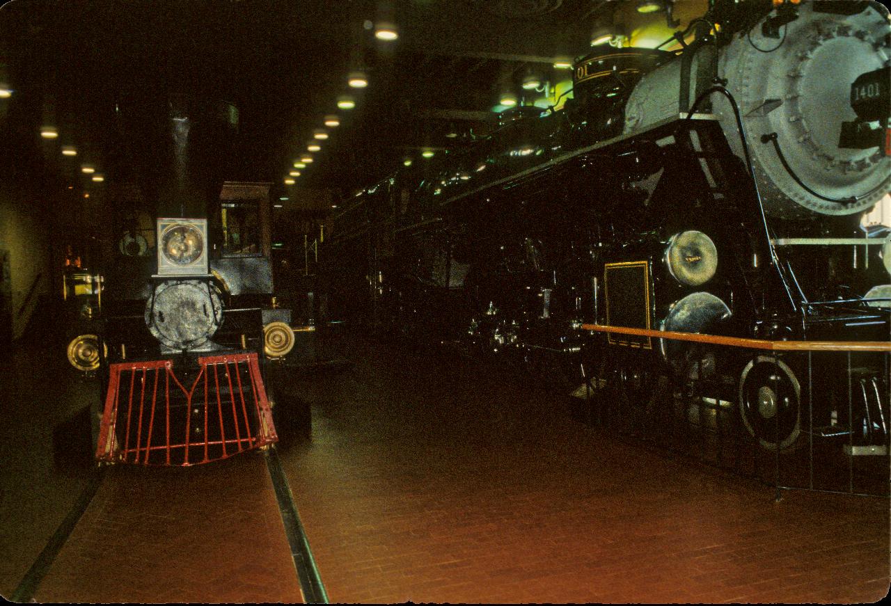 Small, early steam locomotive beside a very large modern one.