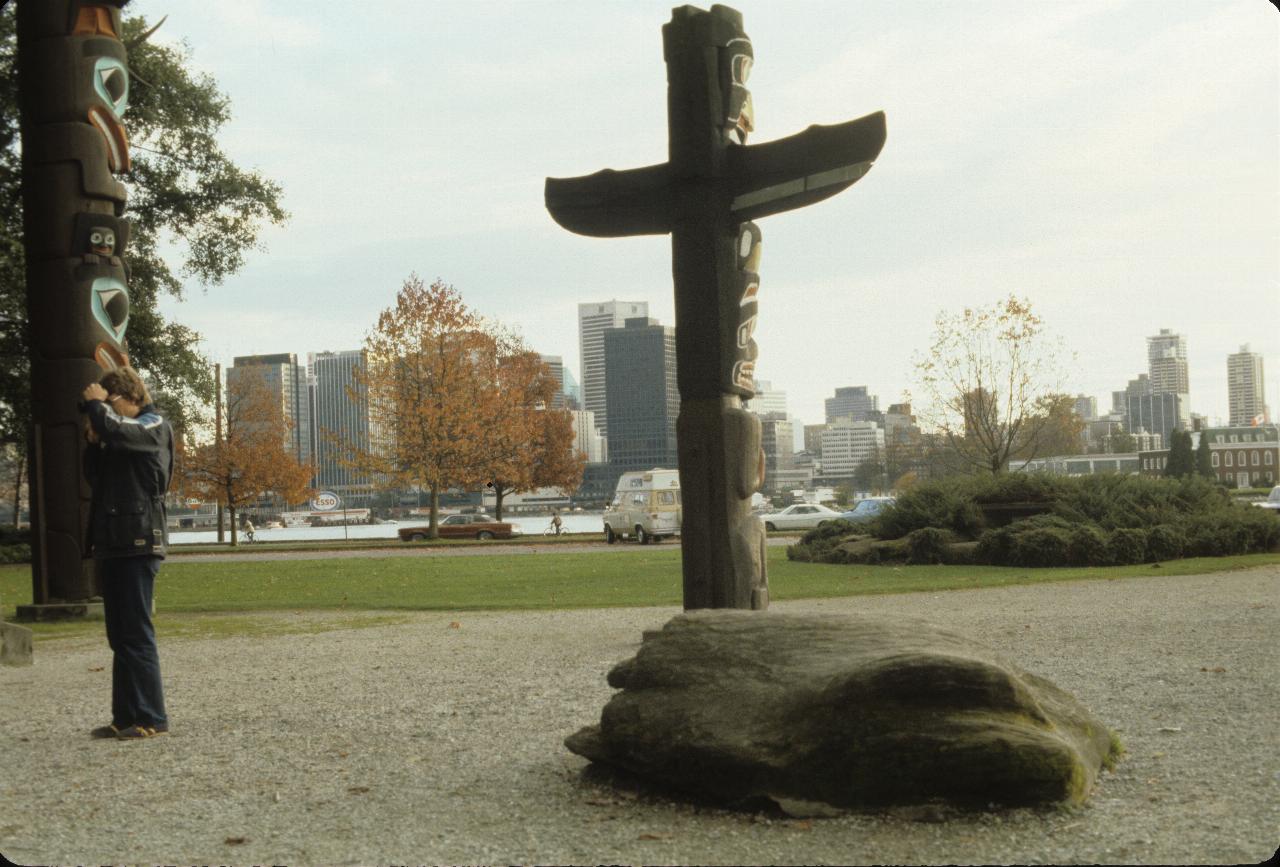 Small totem pole in foreground, with backdrop of Vancouver CBD skyline