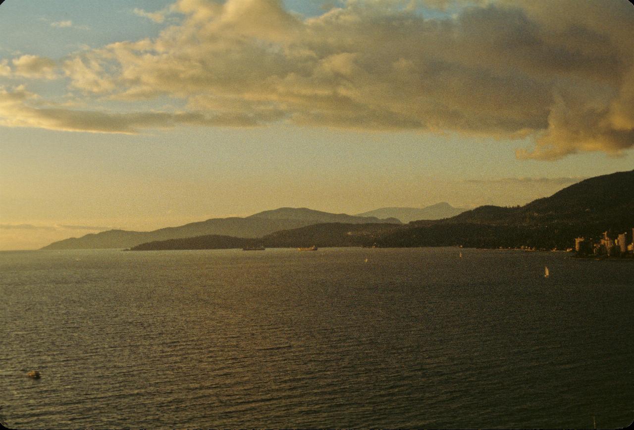 Wide expanse of water to distant mountains, with a few buildings and a couple of ships at anchor