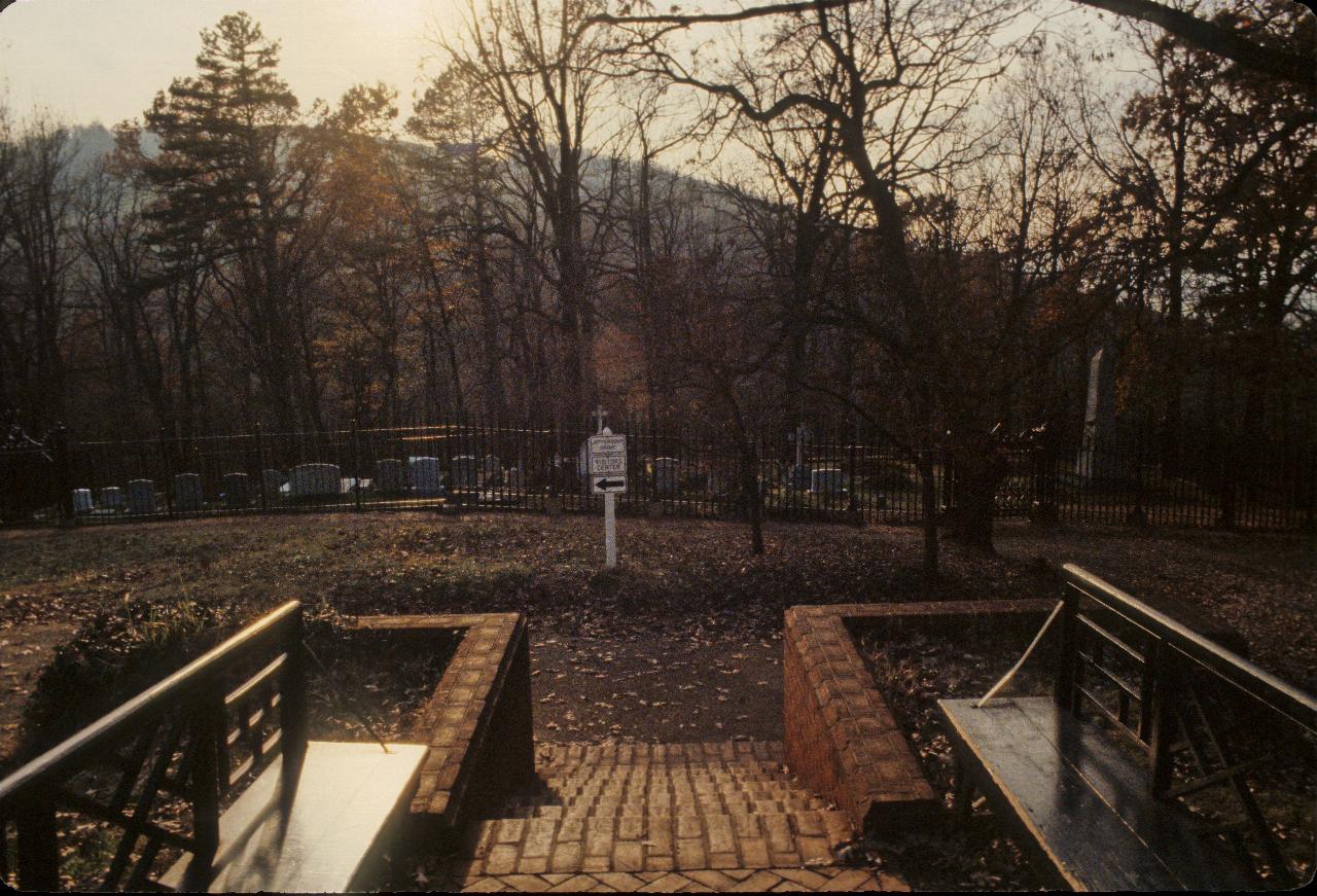 Graveyard with head markers, one obelisk and surrounded by black iron fence.