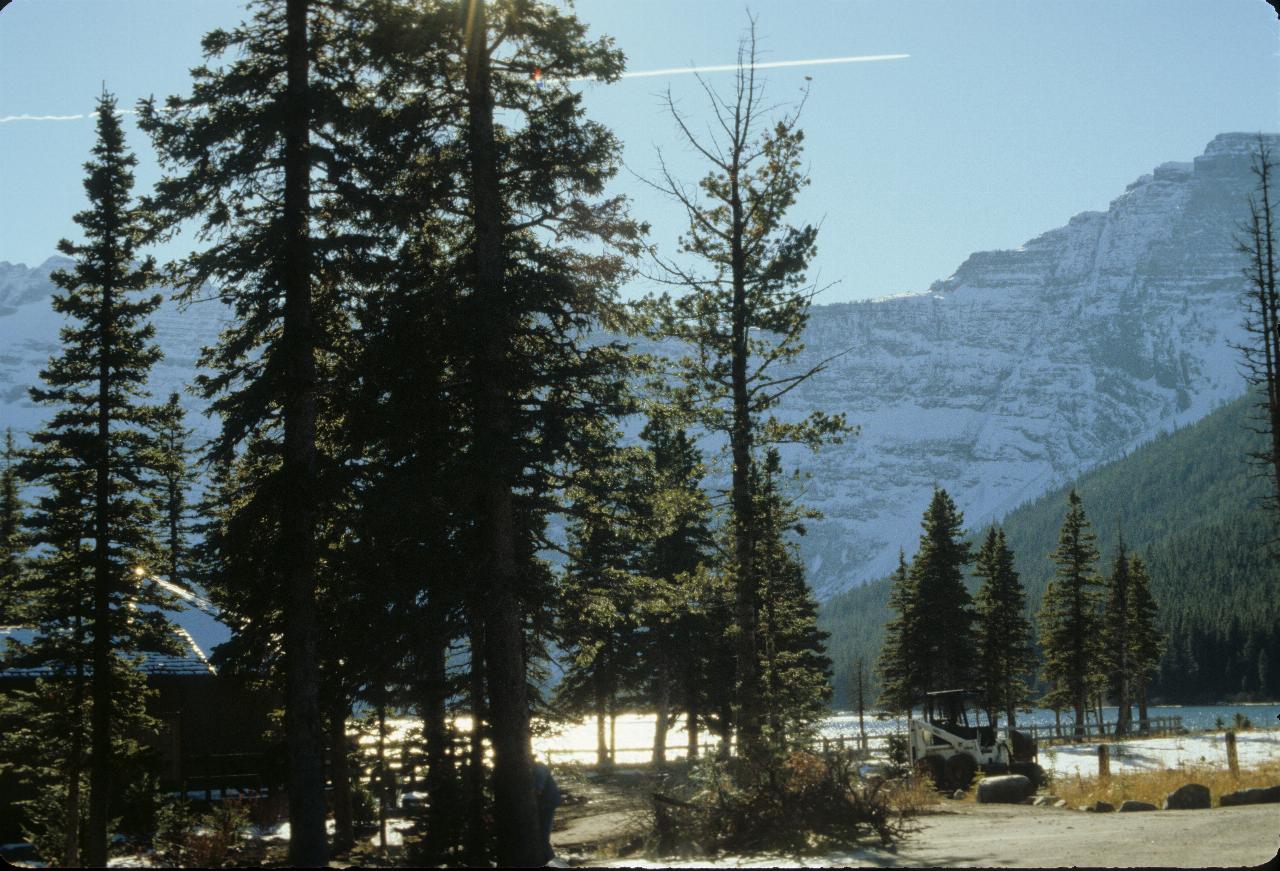 Camp ground by the lake, rugged, snow covered mountains to rear and vapour trail overhead