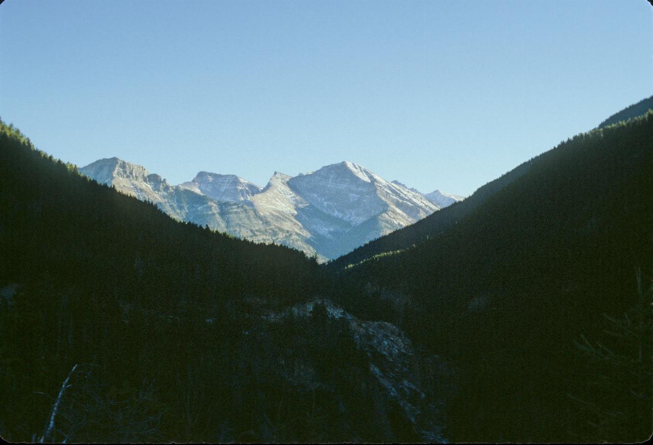 V shaped valley in shade, to snow covered mountains in the sun behind