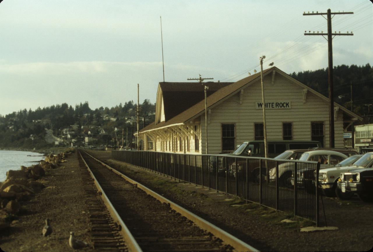 Wooden, light yellow building adjacent to train line adjacent to sea shore