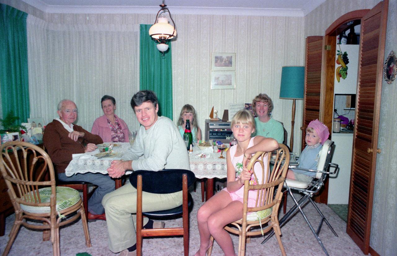 Three generations of people sitting around dinner table