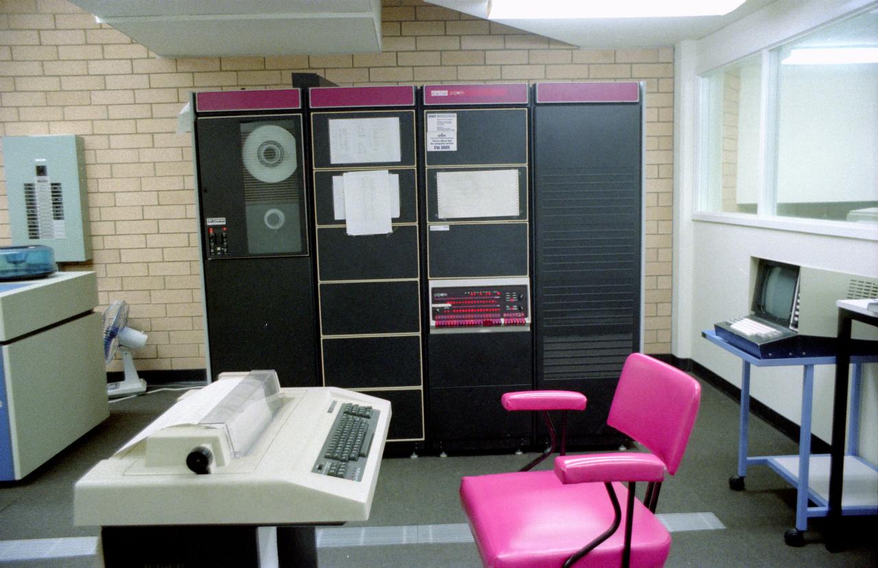 Four section rack of computer equipment; printing terminal in front, bright pin chair