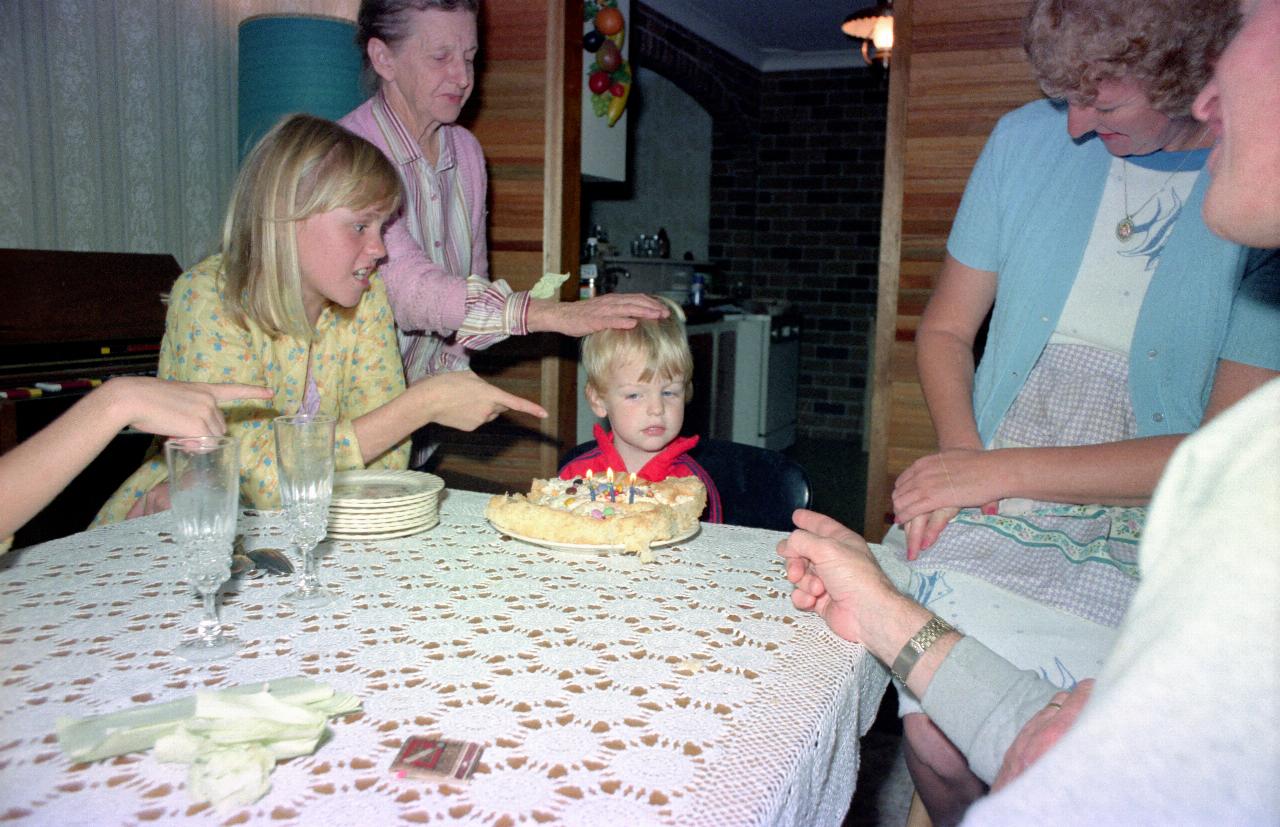 Birthday cake in front of little boy, with others pointing while singing 