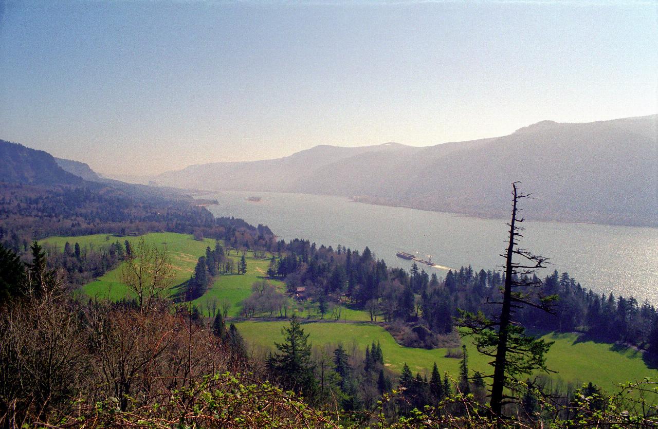 Broad river, viewed from height, wih green fields on this side, barges in river, mountains on far side