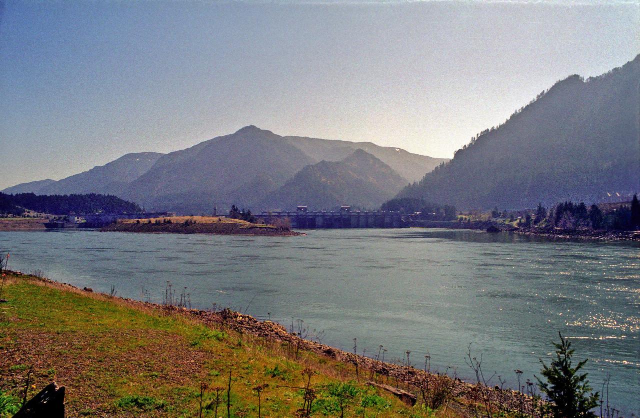 View from river bank of broad river, low dam in the distance, mountains on the other side