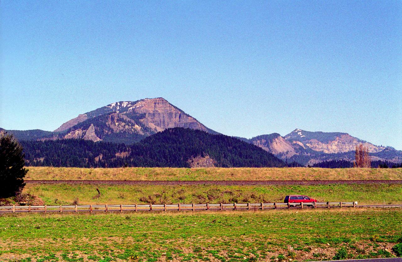 Rugged mountains showing rock strata, train line and passing car