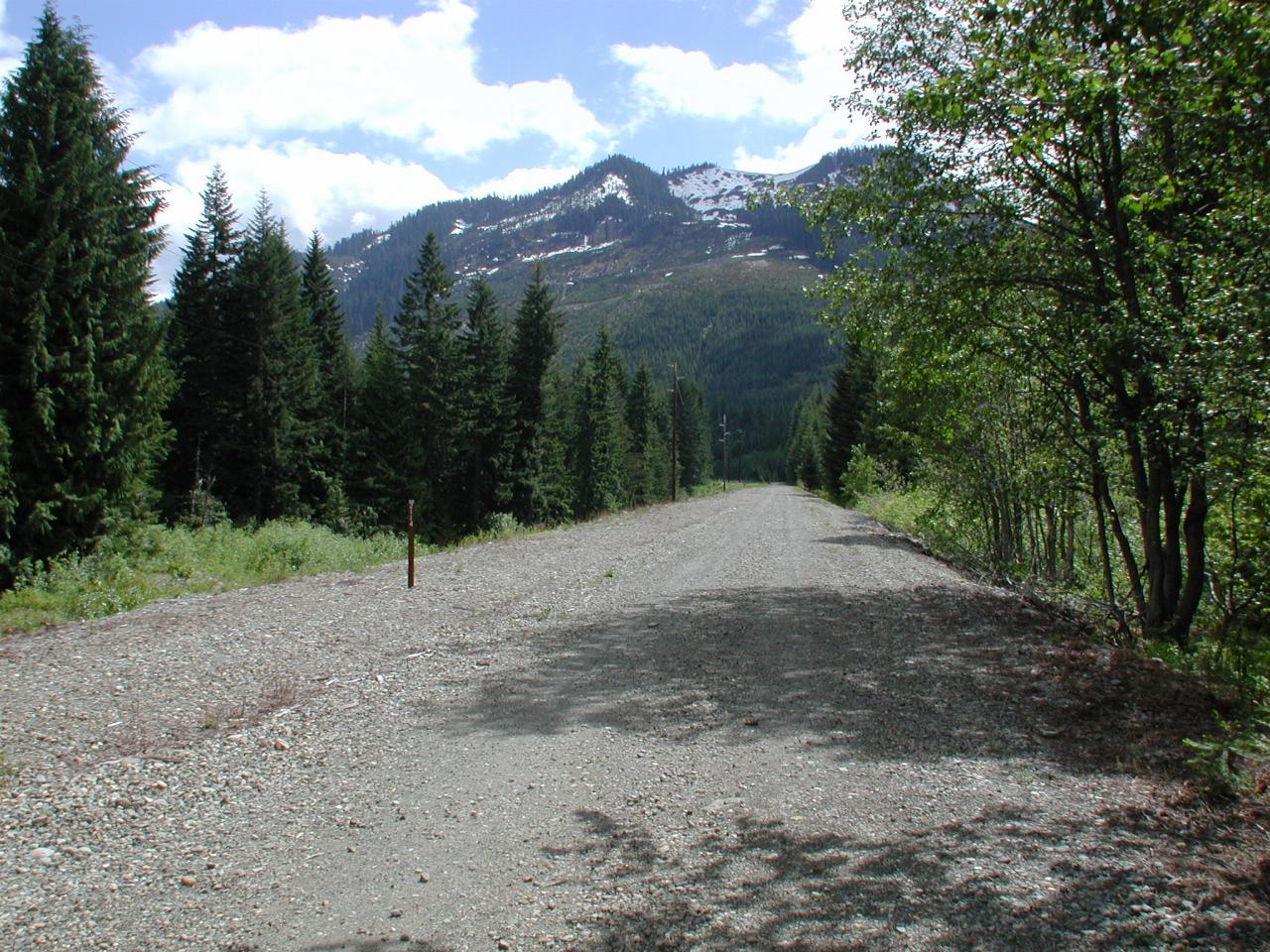 Straight, long gravel path leading away to distant hill with snow on top