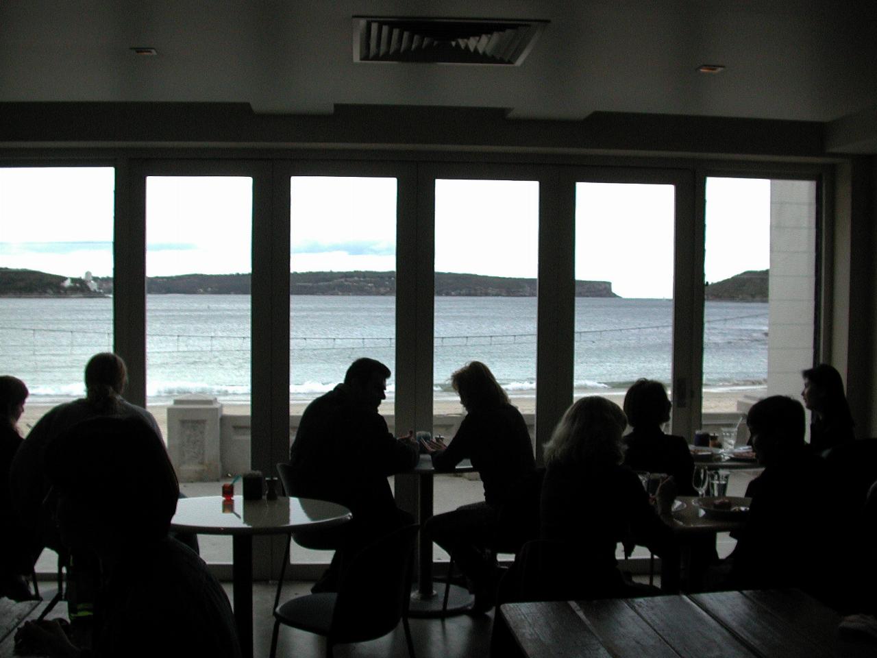 View through glass doors of bay and distant headland, with silhouette of diners inside