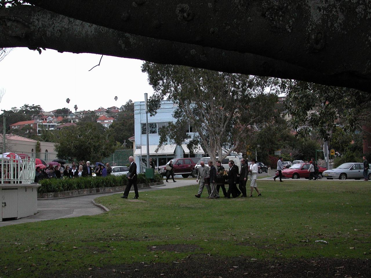 People carrying coffin across grassy park