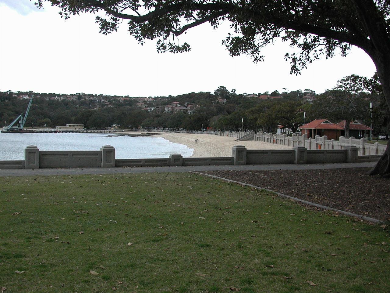 Sandy beach beyond grassy park with cement retaining wall