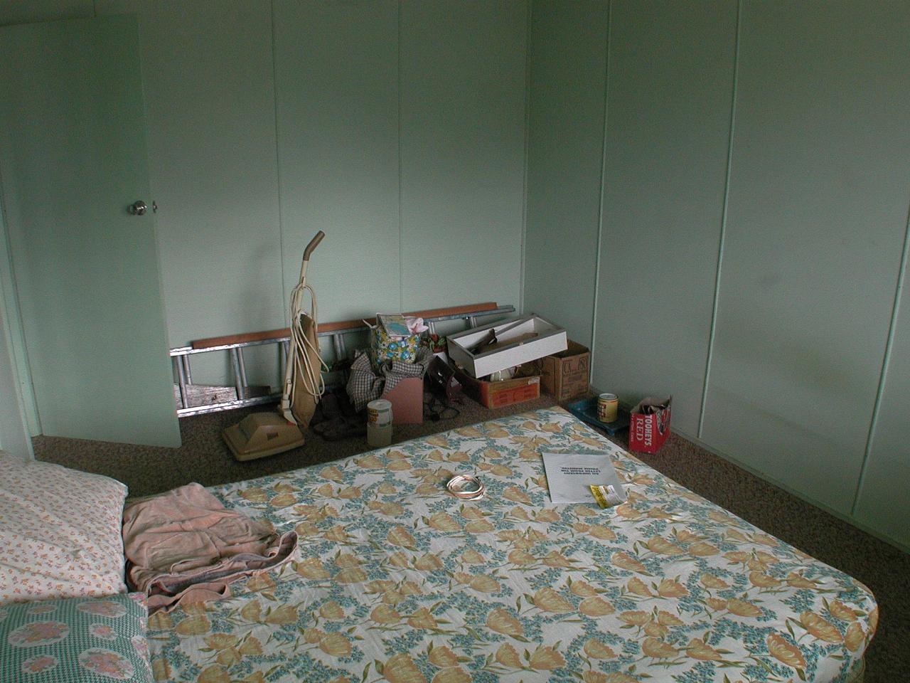 Small room with double bed and cleaning supplies in the corner