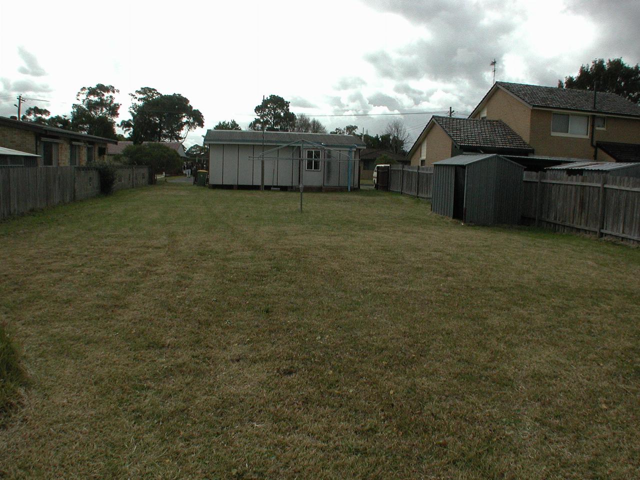 Large grassy yard leading to back of small, fibro cottage