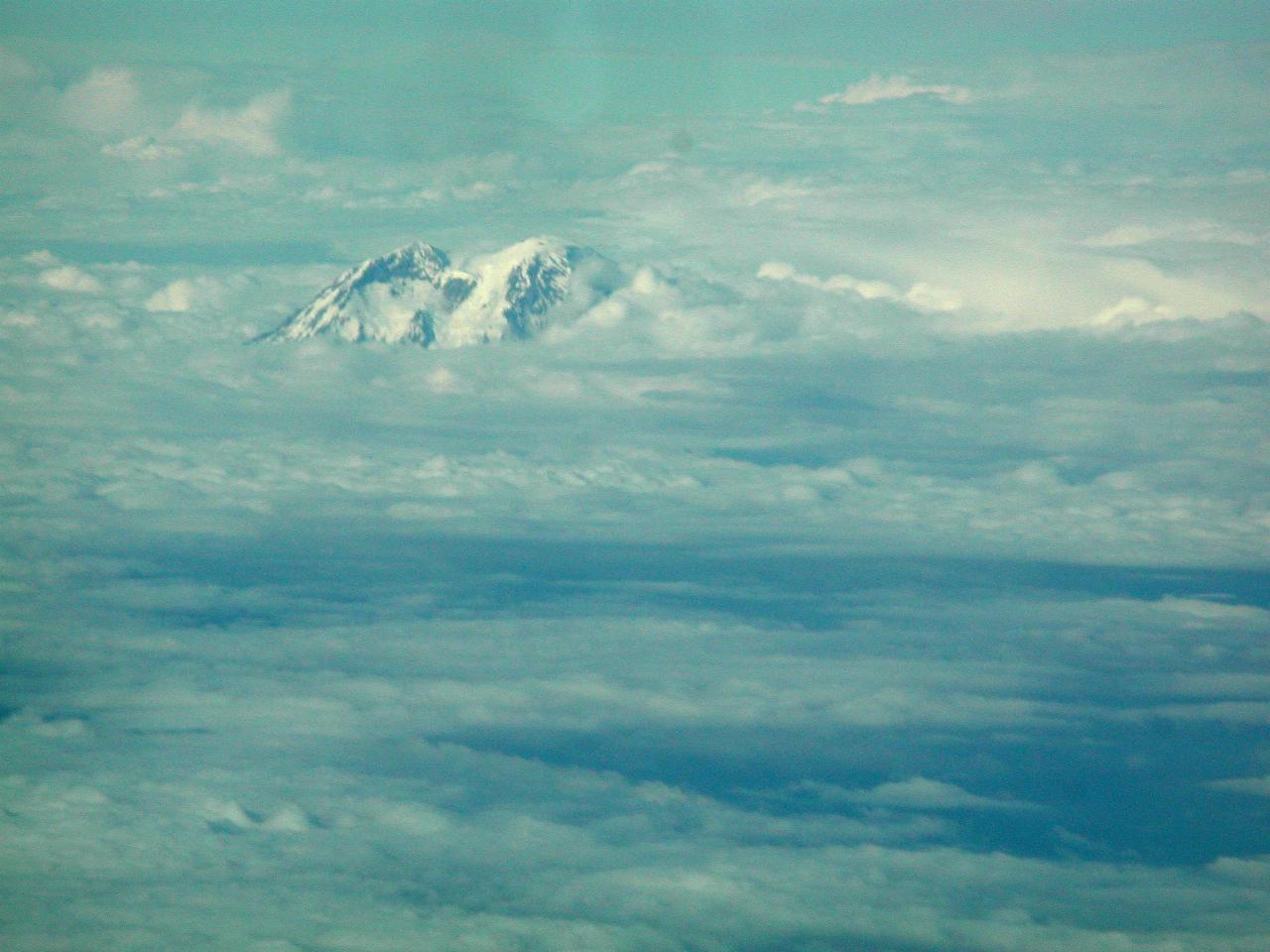 Snow capped mountain appearing above clouds