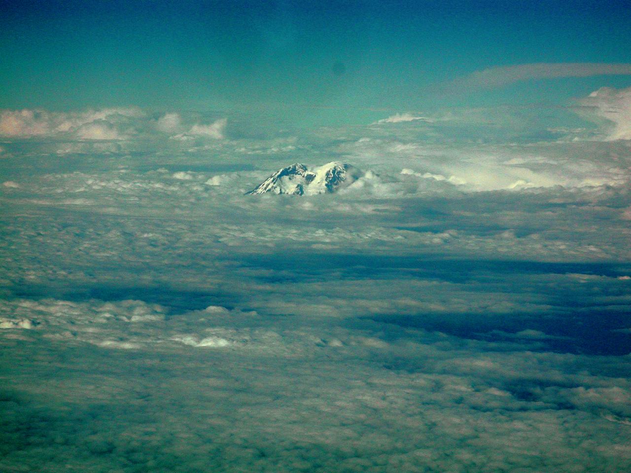 Snow capped mountain appearing above clouds