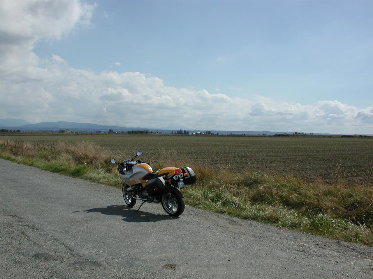 Motorcycle parked at end of road, looking across ploughed field