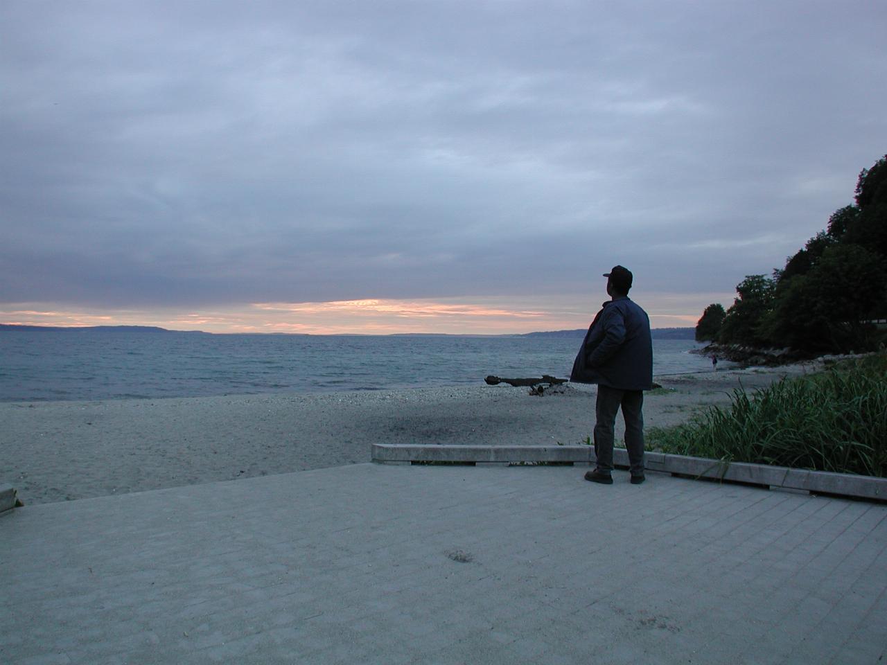 Man standing on beach looking at last sunlight of an overcast sky