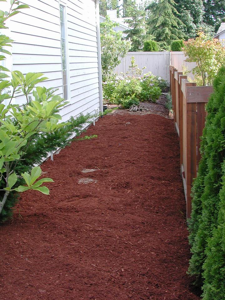 Passage between house and fence with bark