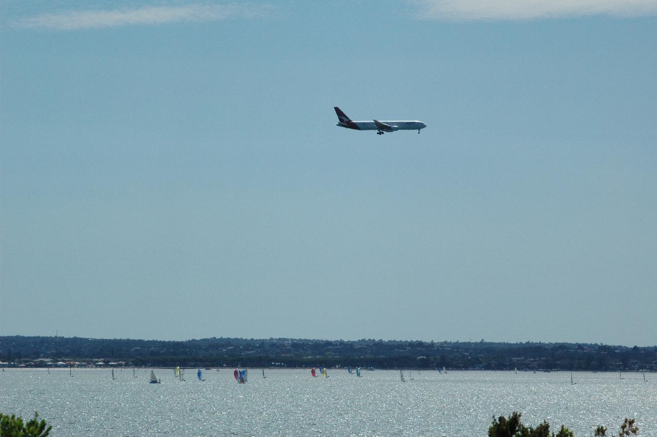 Qantas plane landing at Mascot, as seen from Port Botany with a yacht race on Botany Bay