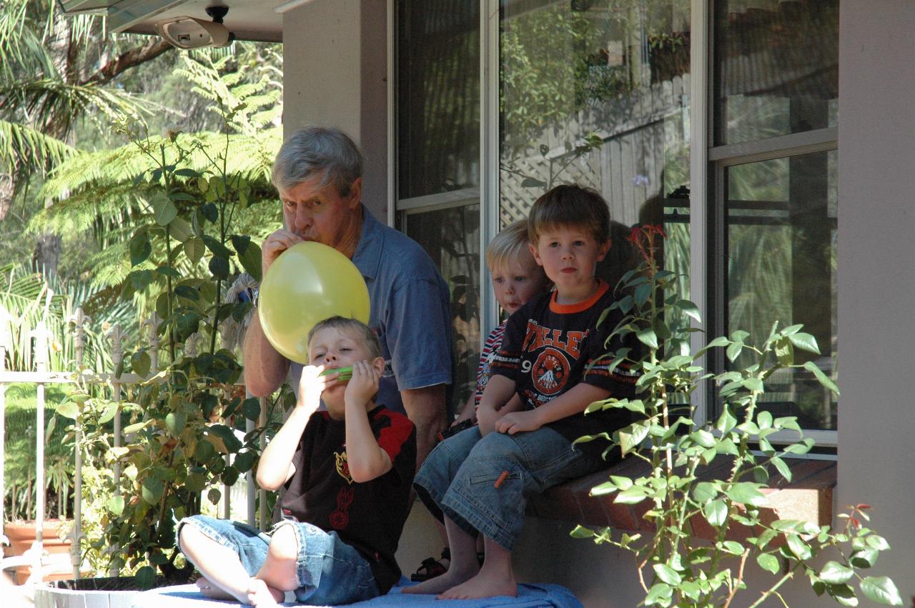 Peter blowing up the balloon, with Flynn and Jake watching, while Tynan plays the mouth organ at Nat's farewell before return to London