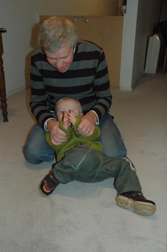 Baby and grandfather on floor, hands joined together to clap