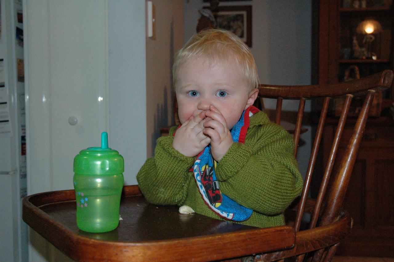 Baby sitting in high chair, hands to mouth