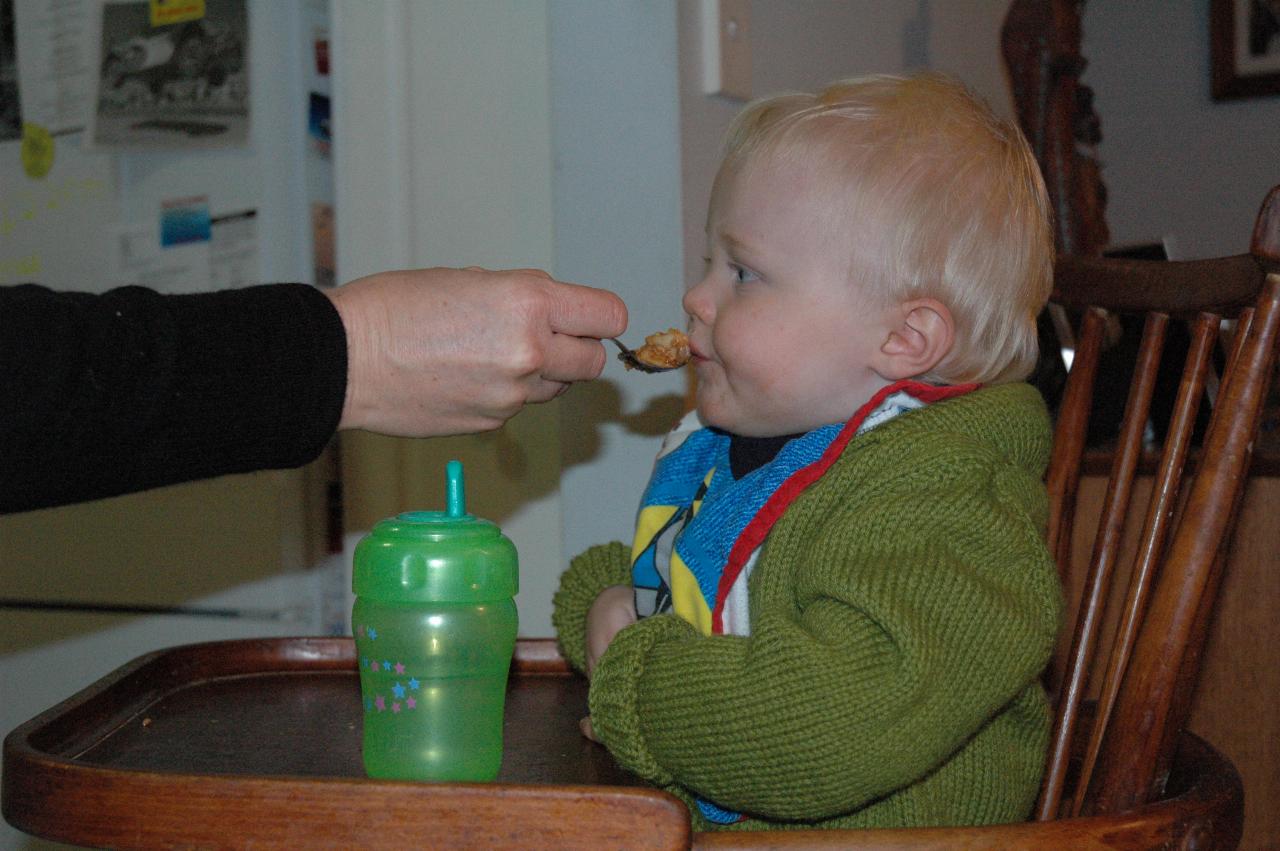 Baby in high chair, mum with spoonful of food at his mouth