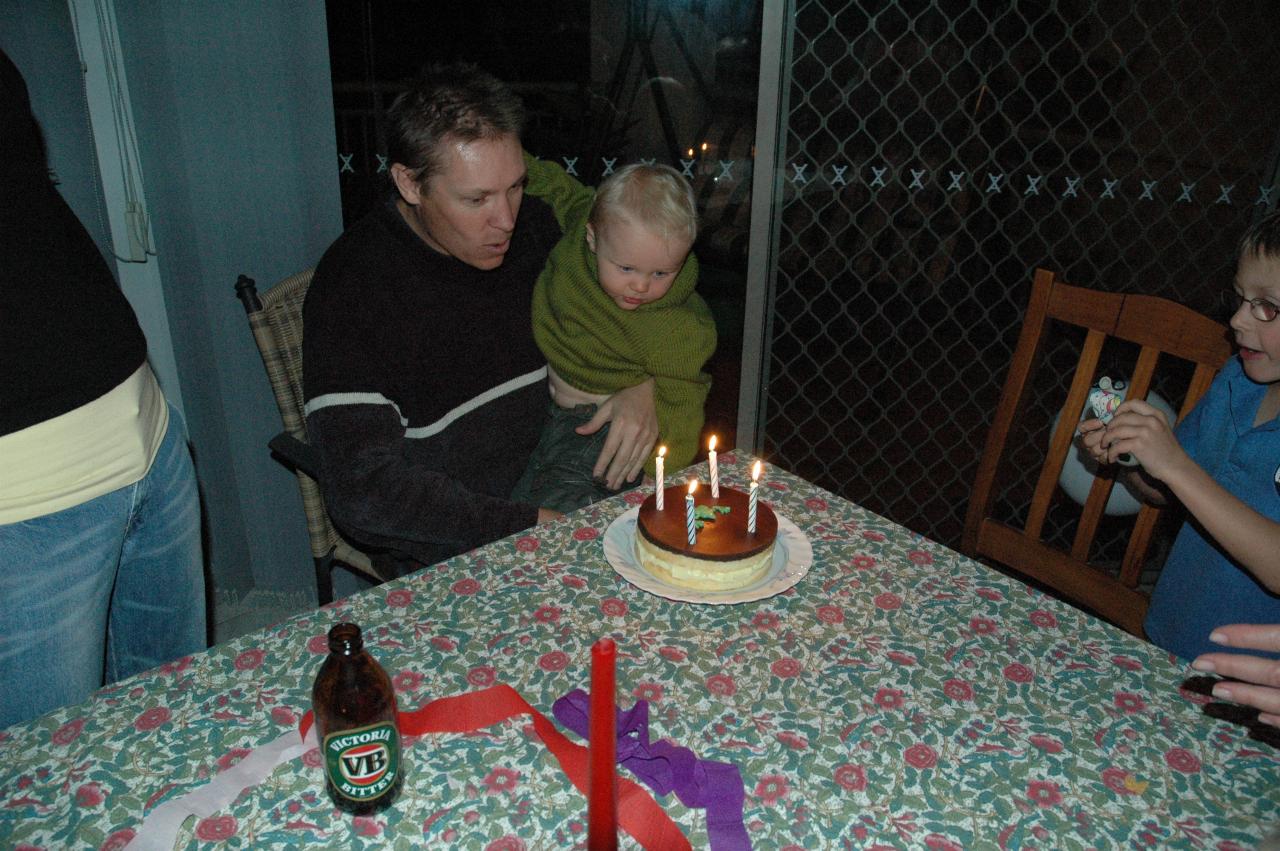 Father with son on lap, looking at birthday cake